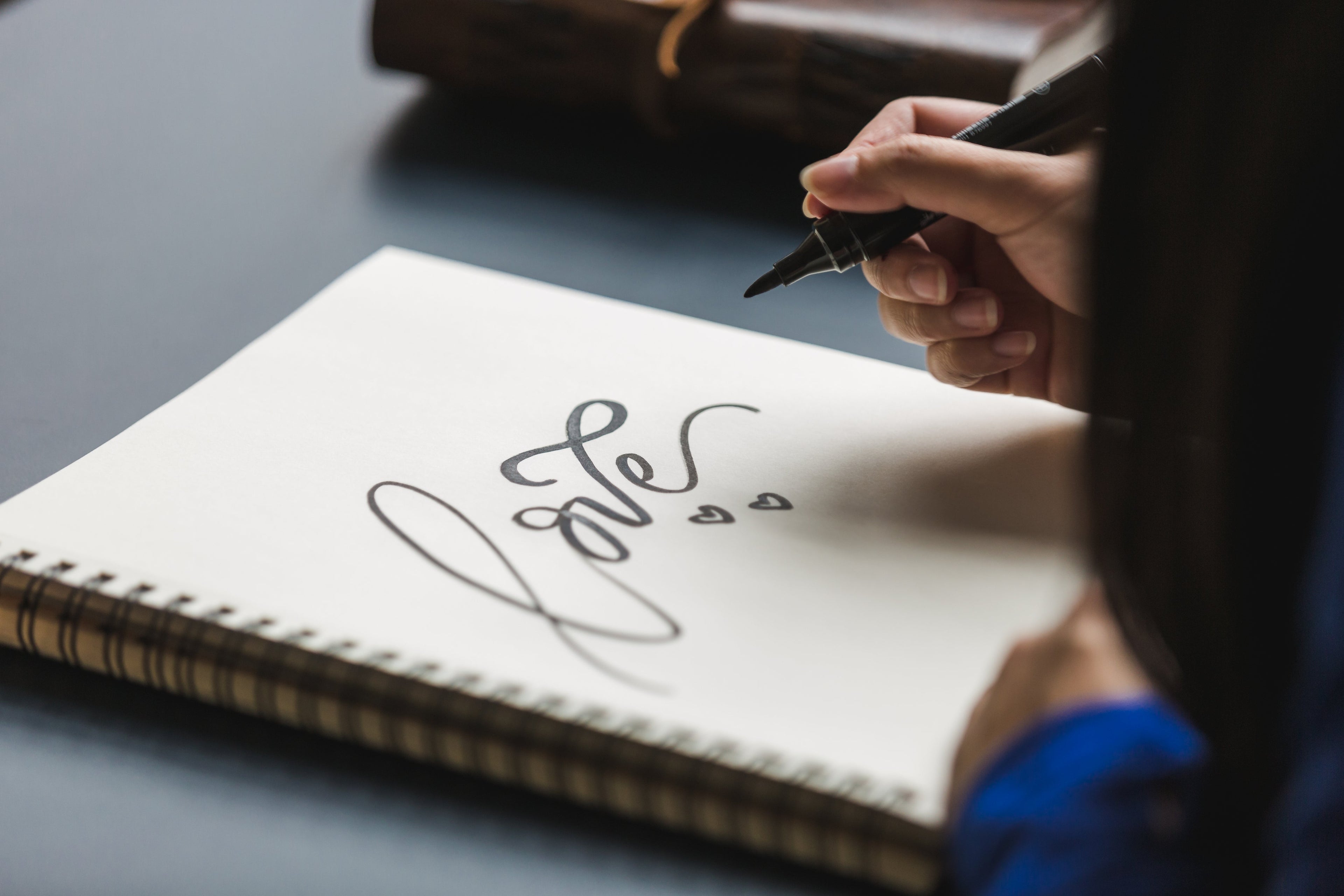 A hand holding a marker pen writing 'Love' on a notebook, symbolizing inspiration for sustainable fashion