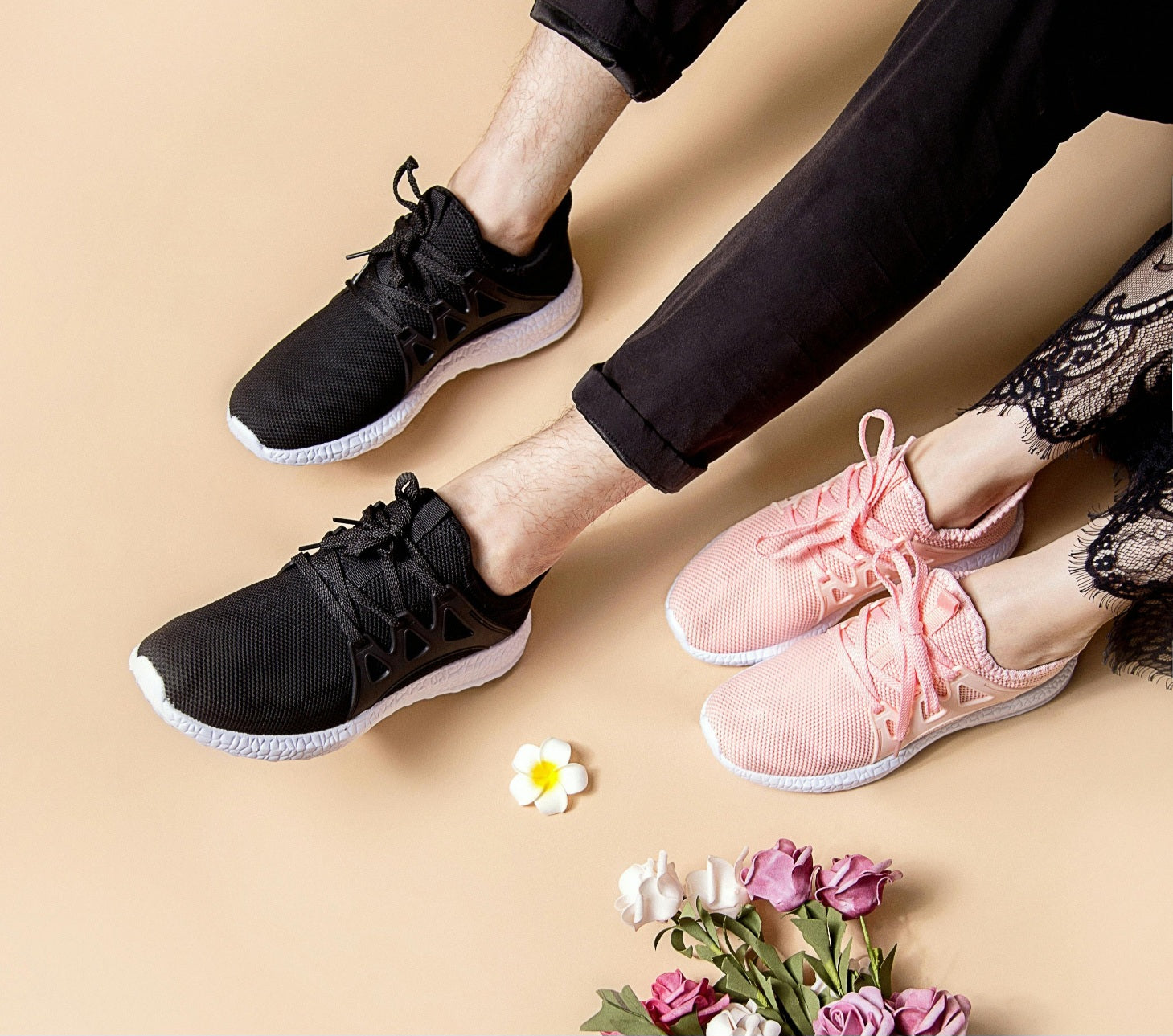 A man and a woman wearing a pair of black and pink sneakers next to pink and white roses, symbolizing for inspiration how to style for unisex fashion